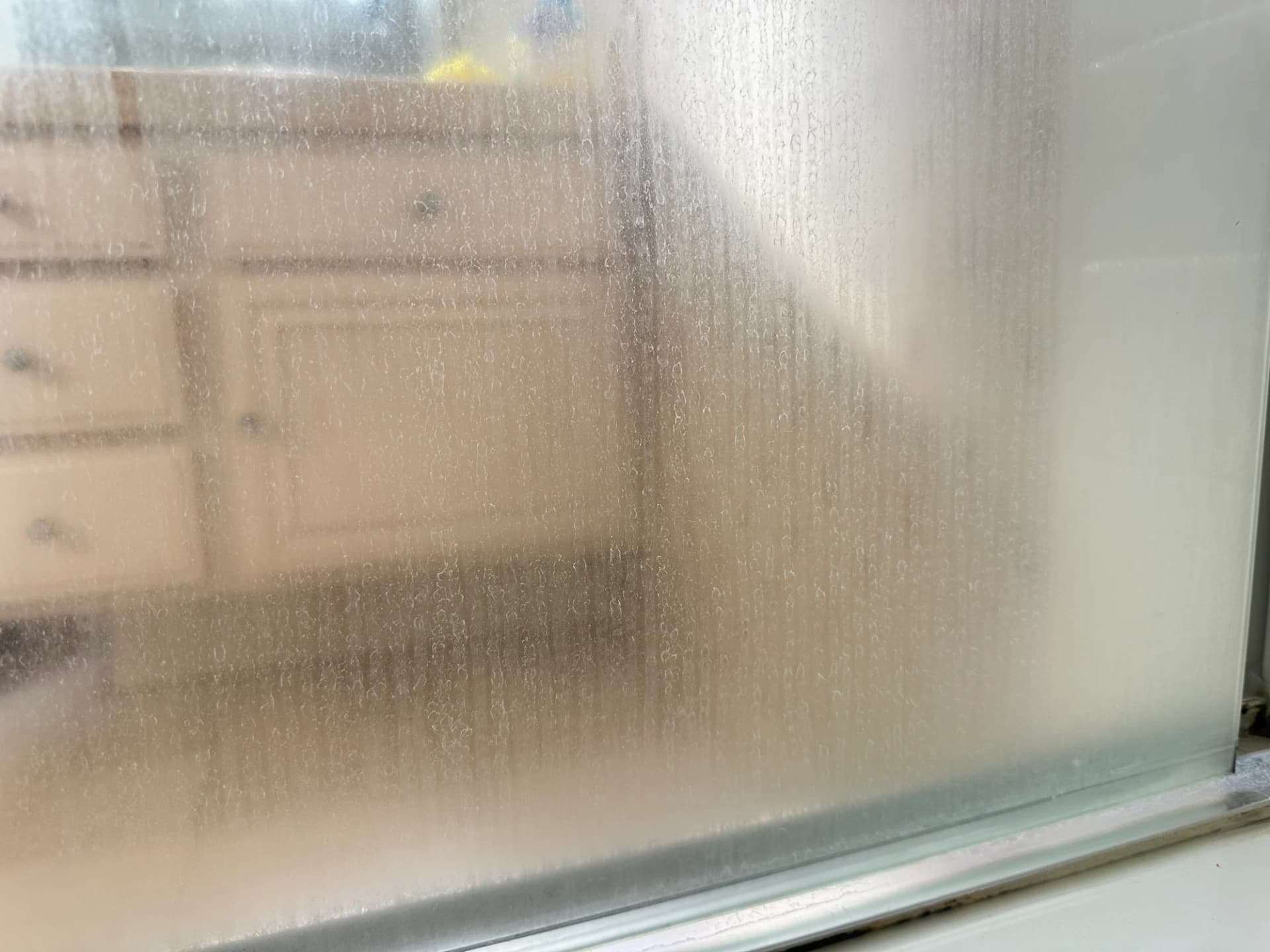 Shower glass door before cleaning — heavy soap scum and water stains blocking the view
