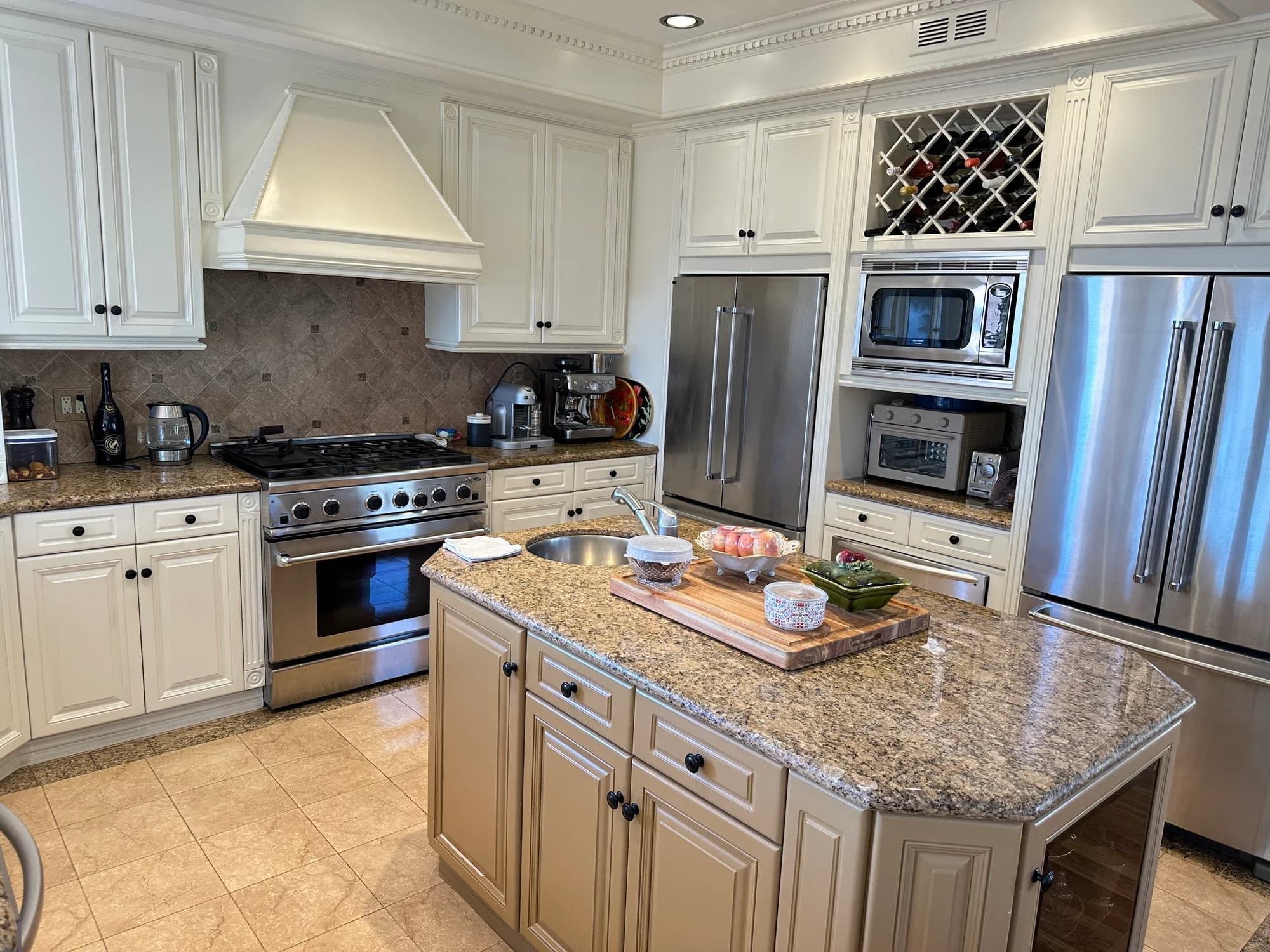Luxury kitchen with white cabinetry, granite island, and stainless steel appliances after professional cleaning