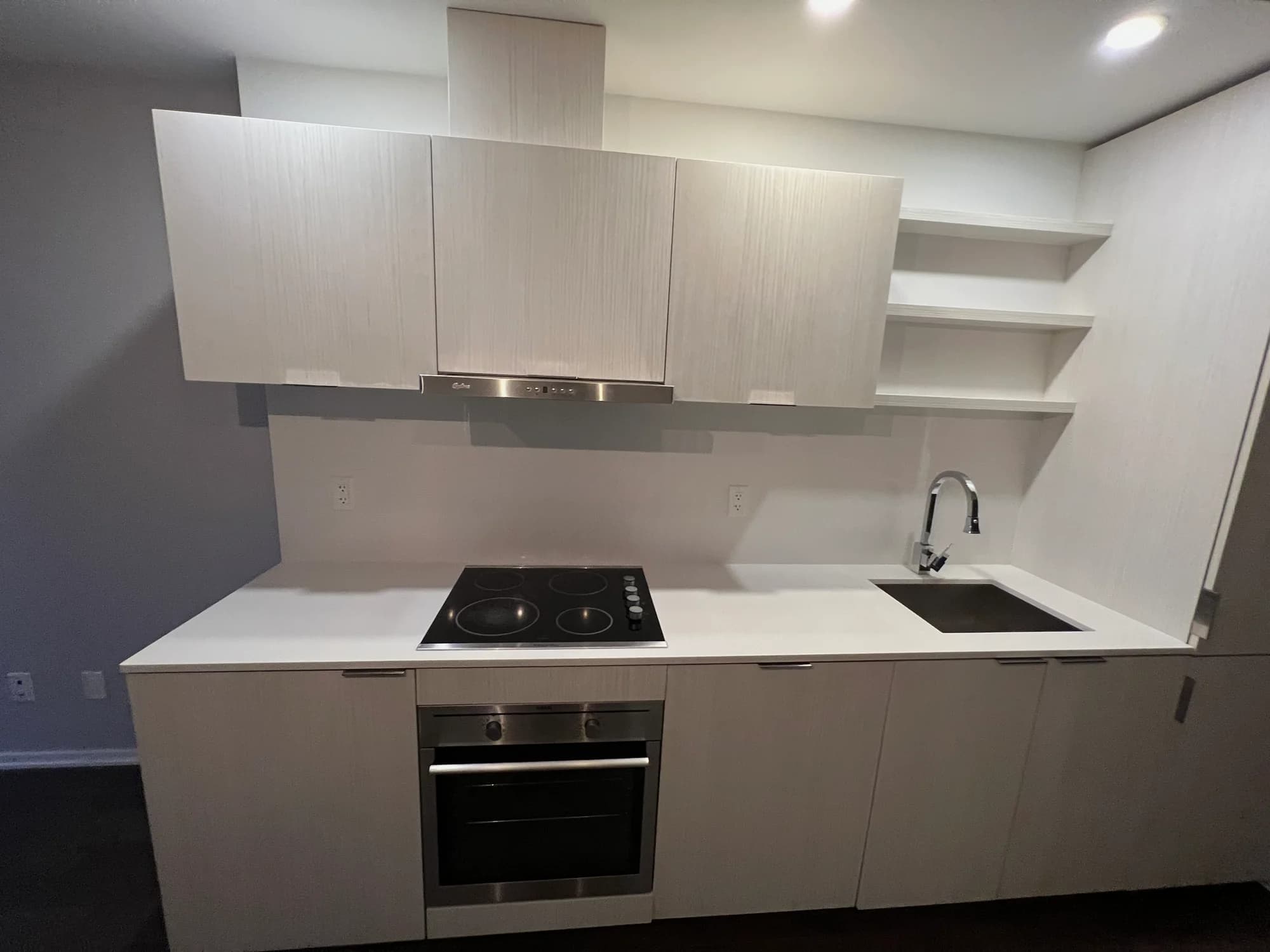 Minimalist kitchen with white countertops, floating shelves, and stainless steel appliances after cleaning