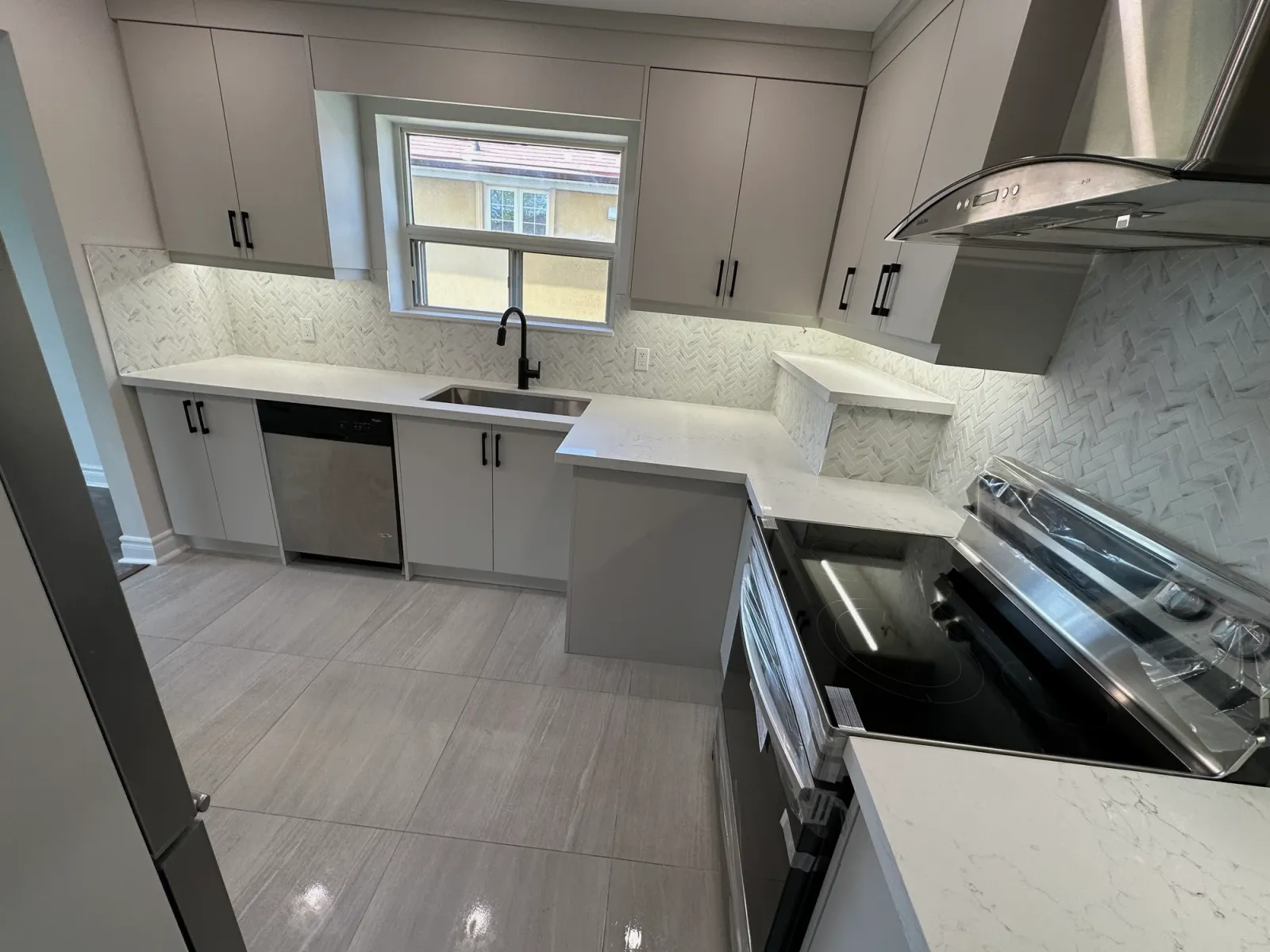 Taupe kitchen with herringbone tile backsplash, black faucet, and gleaming quartz countertops after cleaning