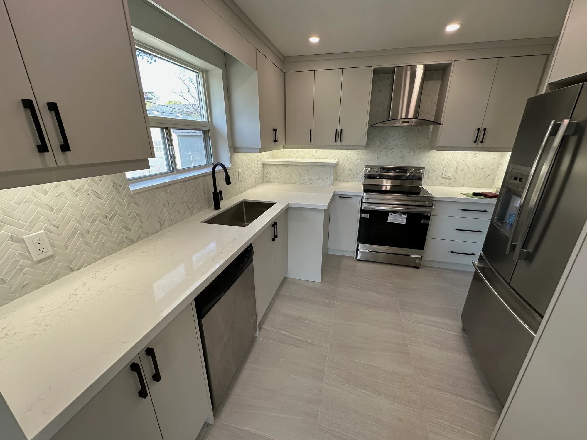 White kitchen with herringbone backsplash, black fixtures, and polished quartz counters after cleaning