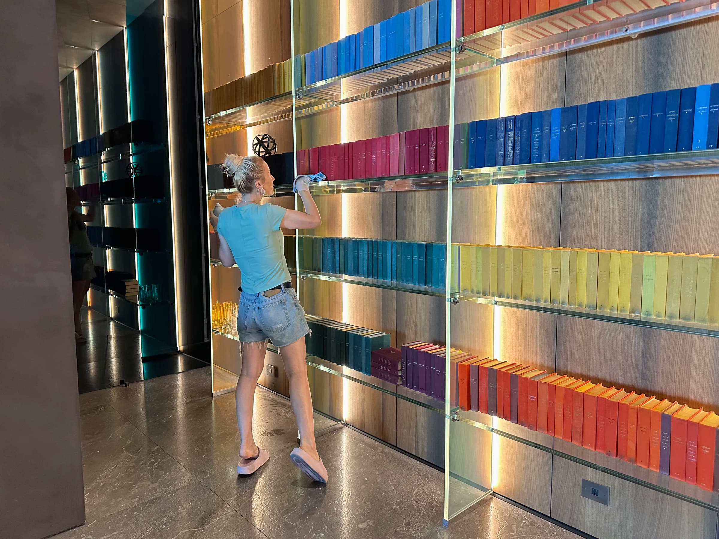 Backlit glass library shelves with color-curated books maintained to a pristine, dust-free standard