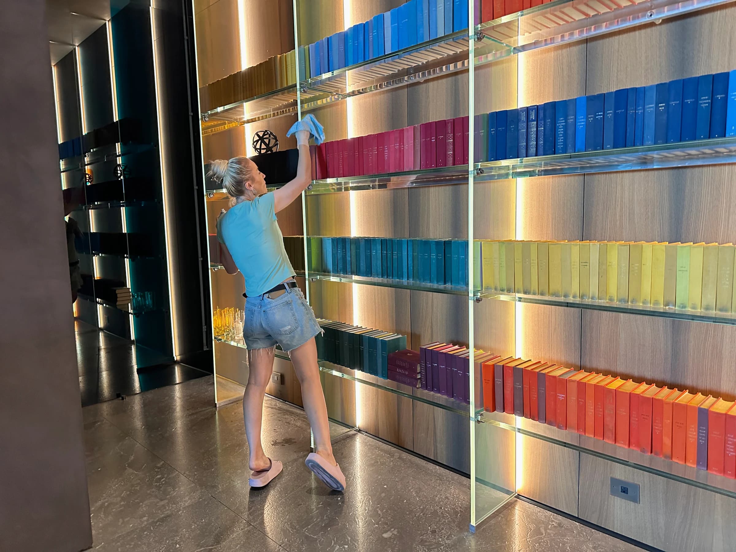 Detailed bookshelf and display cleaning in a modern luxury library with rainbow-organized volumes